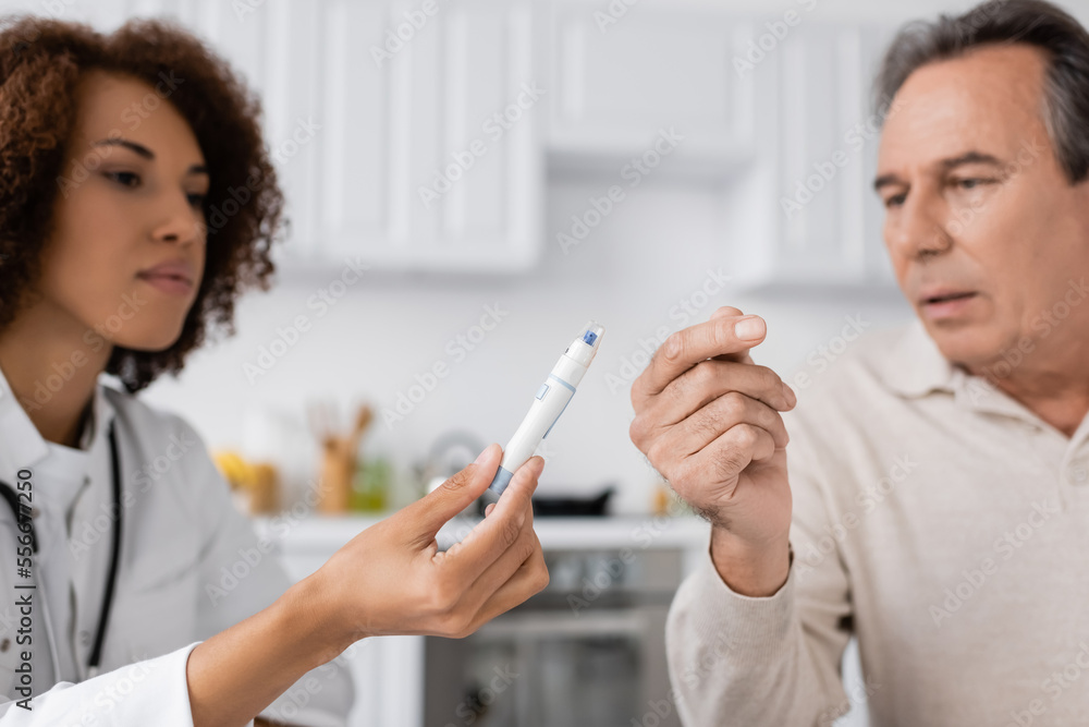 curly african american doctor showing lancet pen to middle aged patient curly african american doctor showing lancet pen to middle aged patient