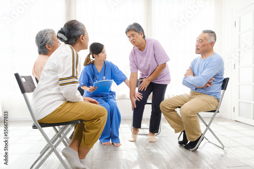 The caregiver therapist sits with a group of Asian senior people in a circle for checking physical and mental health in a group elderly therapy session. The nursing home concept. Vertical image.