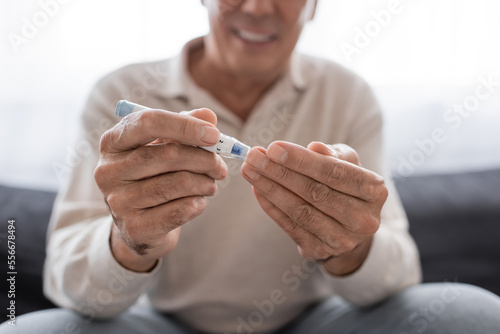 cropped view of smiling middle aged man taking blood sample with lancet pen