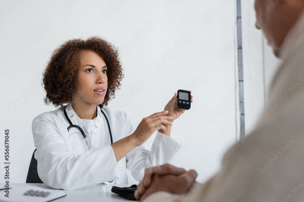 curly african american doctor holding glucose meter device near middle aged man with diabetes in clinic curly african american doctor holding glucose meter device near middle aged man with diabetes in clinic