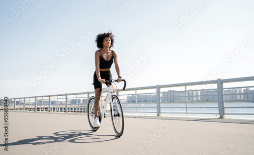 A curly-haired happy woman rides a bicycle. A millennial cyclist rides on environmentally friendly transport in the city.