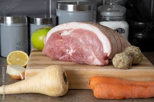 Raw uncooked Leg of Pork joint on a beech block cutting board with seasonable root vegetables cooking apple and sage and onion stuffing balls photo
