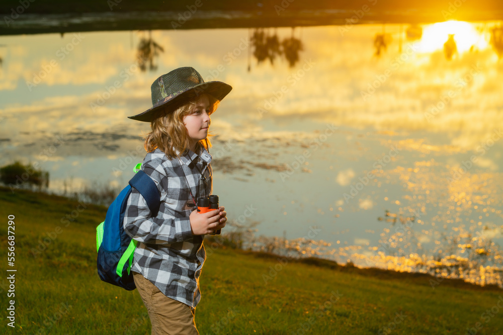 Child with binoculars travelling outdoors. Boy traveler with backpack in a summer day. Portrait of a little boy exploring wildlife. Hiking and adventure concept.