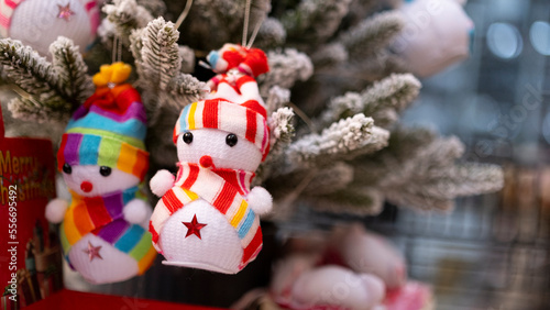 Tiny figurine snowman in colorful outfit in front of snowy pine tree, blurred background, with space and text space