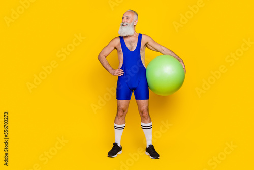 Full length photo of positive cheerful retired man dressed blue overall costume holding fit ball empty space isolated yellow color background