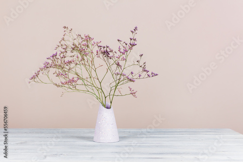 Fotografie Bouquet of dried flowers in a plaster vase on a wooden table against the pale pink wall, front view