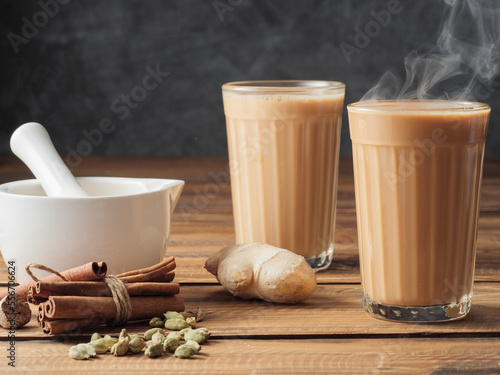 Two mugs of masala tea are on a gray table. Steam comes from them.