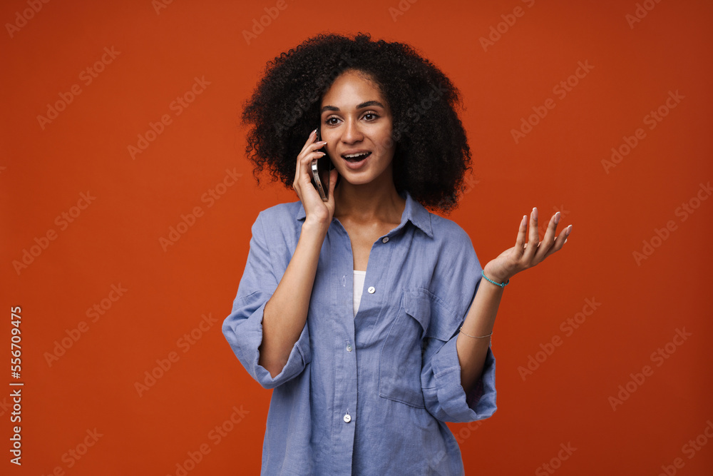 Young african american woman talking on cellphone and gesturing isolated over red wall Young african american woman talking on cellphone and gesturing isolated over red wall