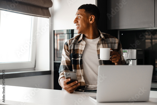 Young african man drinking coffee while using laptop at home