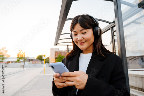 Photo Young woman using cellphone and headphones standing on bus station