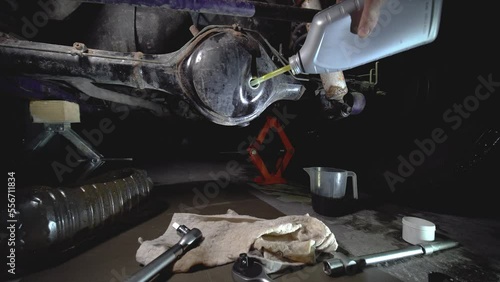 Pours new oil in the front differential of an off-road vehicle, truck with four-wheel drive. Car service. Tools and spare parts.	
