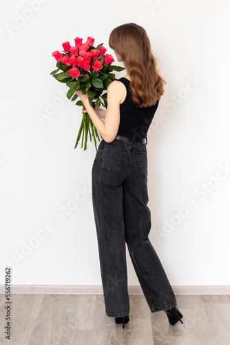 Young attractive girl with a bouquet of red rosesin full growth on a white background, back view.  The concept of happiness, joy and celebration photo