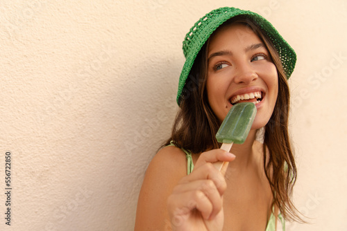 Positive young caucasian woman loks away eats ice-cream with great mood. . Model with brunette wavy hair wears panama and sundress. Concept of fun, positive moments.