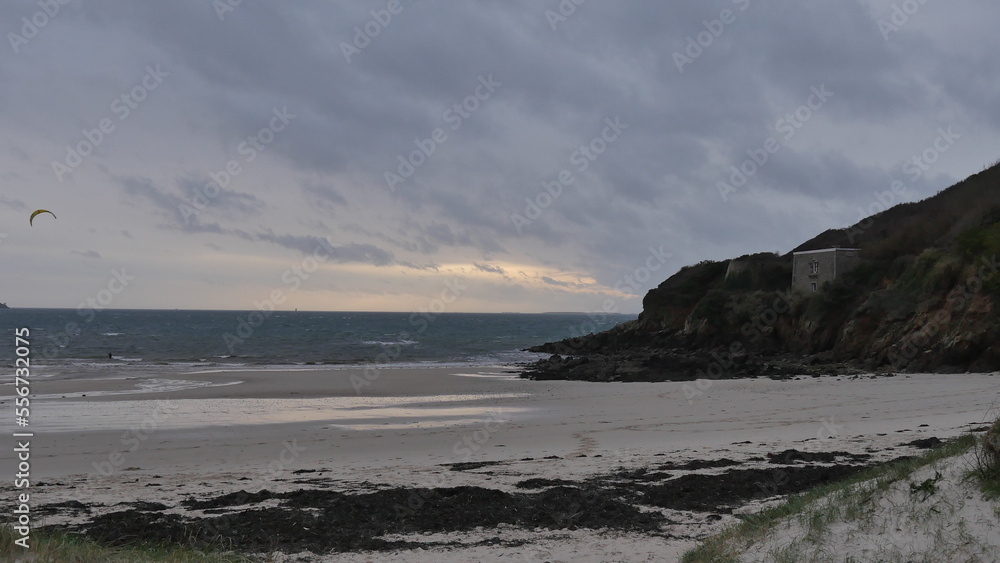 Plage bretonne sous un ciel nuagueux, gris et menaçant, mer agitée, couché soleil, début de soirée, promenade côtière, un peu de vent, de la nature et végétation maritime ou cotière