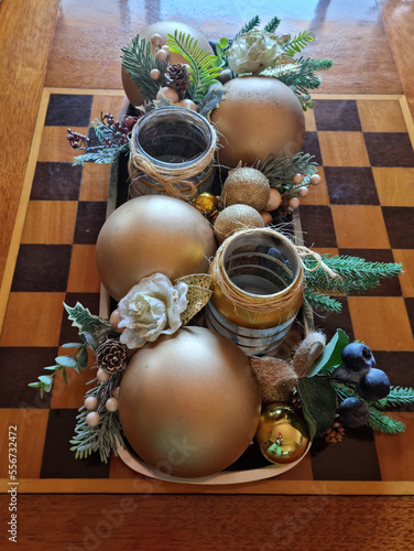 Christmas arrangement with golden balls and flowers on a chessboard.