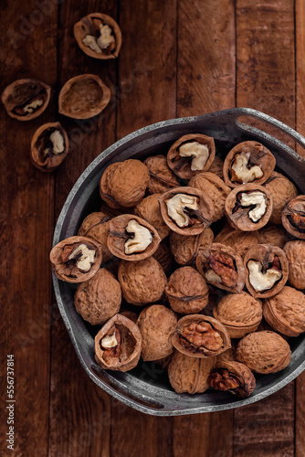 Fresh walnut kernels and whole walnuts in a metal bowl on a dark wooden background.