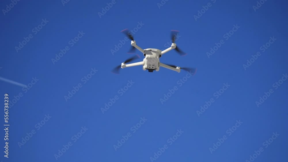 View from ground of flying quadrocopter against cloudless blue sky. Low-angle view of remote controlled drone with flying in air. Shooting in slow motion. View from ground of flying quadrocopter against cloudless blue sky. Low-angle view of remote controlled drone with flying in air. Shooting in slow motion.