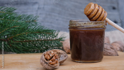 Miel orgánica casera de color marrón oscuro en un tarro de cristal con palito mielero en un fondo rústico con nueces con cáscara y hojas  photo