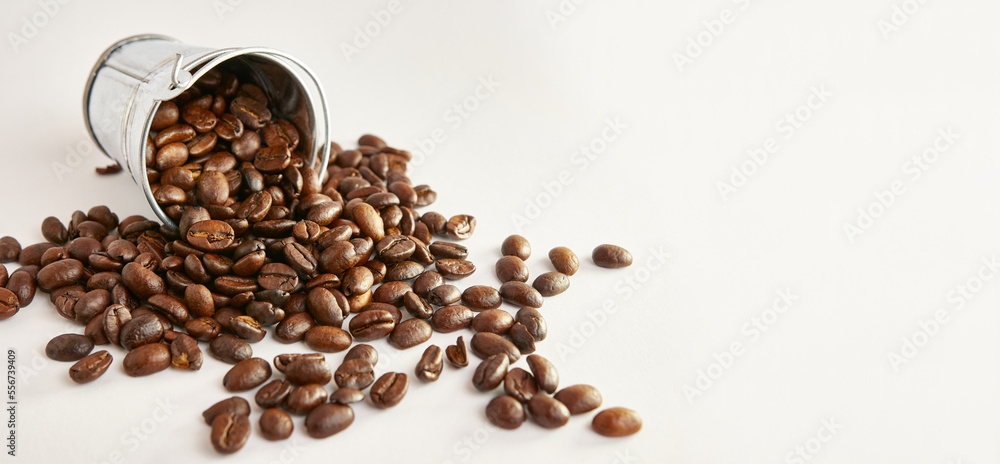 A metal bucket with a pile of scattered roasted coffee beans. A metal bucket with a pile of scattered roasted coffee beans.