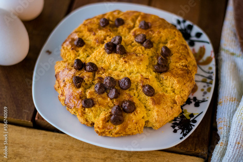 Delicious cornbread with chocolate chips, placed in a white porcelain dish and composed with eggs, wooden spoon, whisk, white cloth and a cup of coffee