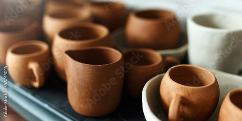 A close-up of various drying clay tableware on a shelf. A pottery studio concept. Craftmade dishes, bowls, pots, mugs of different colors. Cozy view. workshop with ceramic dishware photo