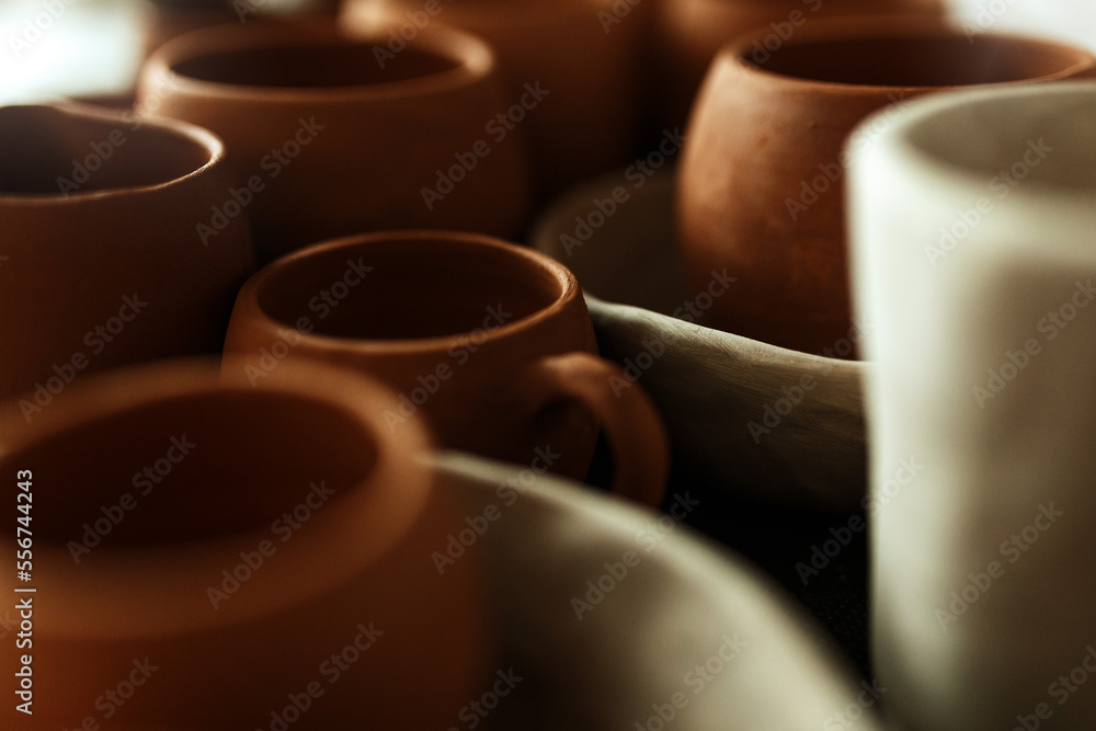 A close-up of various drying clay tableware on a shelf. A pottery studio concept. Craftmade dishes, bowls, pots, mugs of different colors. Cozy view. workshop with ceramic dishware A close-up of various drying clay tableware on a shelf. A pottery studio concept. Craftmade dishes, bowls, pots, mugs of different colors. Cozy view. workshop with ceramic dishware