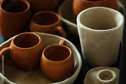 A close-up of various drying clay tableware on a shelf. A pottery studio concept. Craftmade dishes, bowls, pots, mugs of different colors. Cozy view. workshop with ceramic dishware