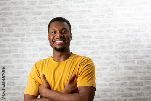 Indoor portrait of young black man standing in black shirt with crossed arms, smiling and looking at camera