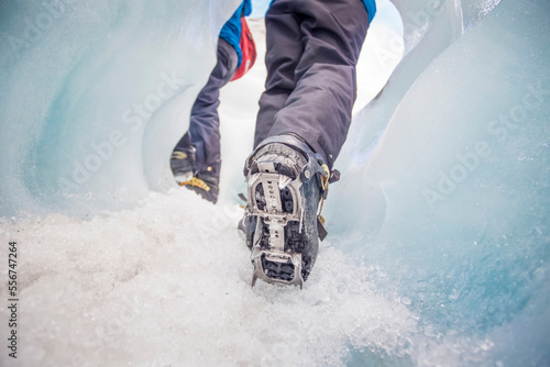 Close-up of person's feet wearing spiked traction cleats while walking on ice through the famous Franz Josef Glacier; West Coast, New Zealand photo