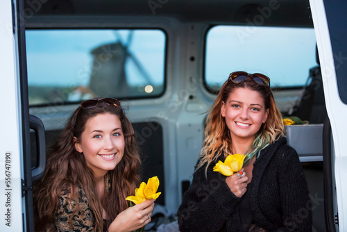 Two young women holding yellow tulips with a windmill in the background, Egmond aan Zee, Holland photo