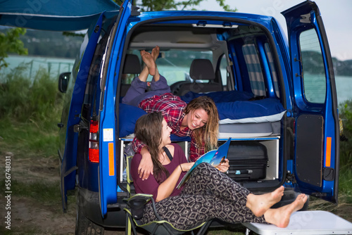 Campsite set up along Lake Balton for the day with travelers hanging out in camper van looking at magazine; Zamardi, Somogy County, Hungary photo