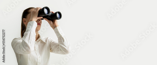 Young woman in a white shirt looks through binoculars on a white background. Banner
