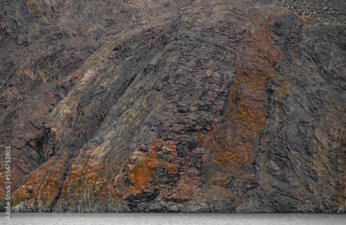 Iron oxide rich rocks on a craggy rockface at the water's edge; Nunavut, Canada photo