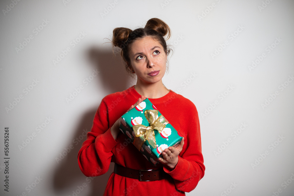 Portrait of young attractive brunette woman with bundles in red pullover trying to guess what is inside the present green Christmas box Portrait of young attractive brunette woman with bundles in red pullover trying to guess what is inside the present green Christmas box