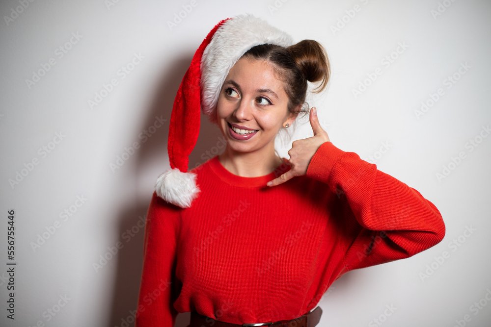 Portrait of young attractive brunette girl with two bundles in red pullover and Santa hat showing call me symbol Portrait of young attractive brunette girl with two bundles in red pullover and Santa hat showing call me symbol