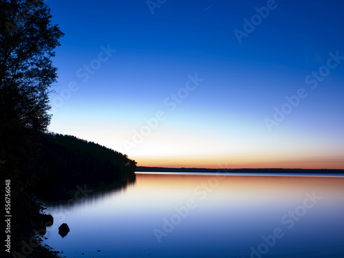 Glowing horizon at sunset reflected in tranquil water of Gregoire Lake; Fort McMurray, Alberta, Canada photo