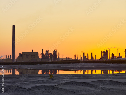 Golden sunlight behind the silhouetted structures at oil sand production facility (Suncor Energy) at sunset; Fort McMurray, Alberta, Canada