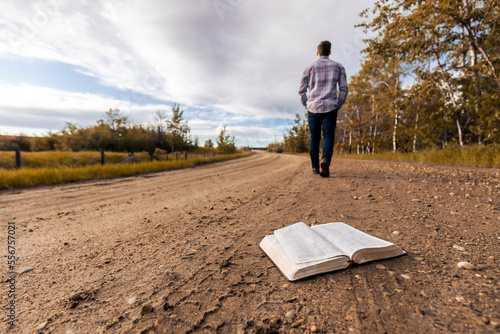 A young man walks down a country road away from Bible laying open;  Alberta, Canada photo