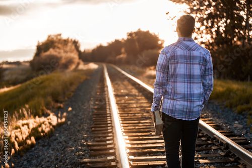 A young man stands on train tracks holding his Bible and looking up the tracks; Alberta, Canada photo