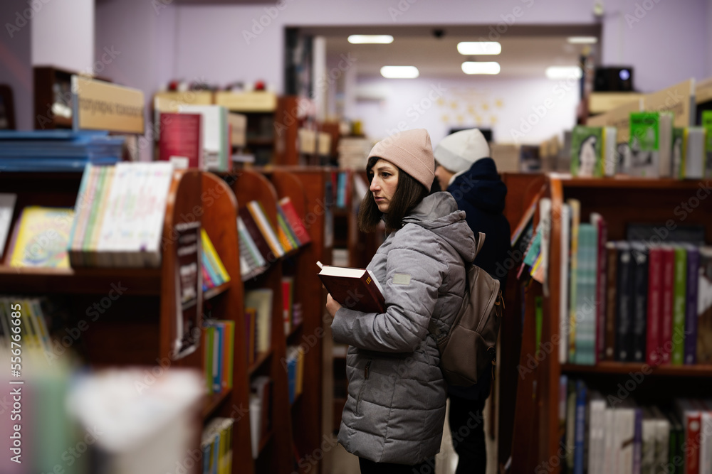 Mother with son in jacket and backpack reaching a book from bookshelf at the library. Mother with son in jacket and backpack reaching a book from bookshelf at the library.