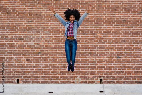 Young, Latina, Hispanic, African-American Haitian woman with curly hair screaming and jumping with victorious arms. © juanpablo