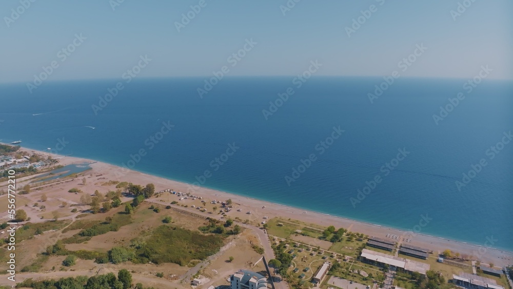 Top view of the coastline. Sea and sandy beach. Houses and hotels by the sea. Sun loungers and umbrellas on the beach.