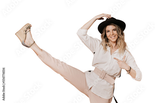 Charming smiley blonde in a hat with a brim, white blouse and light pink pants makes kick with her leg, knocking down imaginary discount number, over transparent background. Sales and shopping concept photo