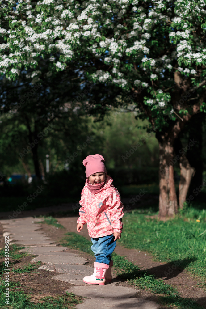 A little girl stands on a path in front of a flowering tree with white flowers. Laughs. A little girl stands on a path in front of a flowering tree with white flowers. Laughs.
