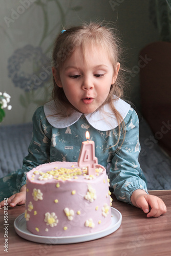 A little girl of four years in a blue dress, celebrates a birthday with a cake on the table. Blows out the candles. Vertical orientation.