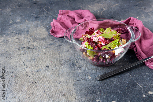 beetroot and feta cheese salad in glass bowl, fork on blue background, copy space