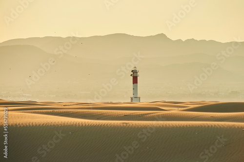 Lighthouse with red stripe on the rippled sand dunes in the evening light at sunset, Ebro River Delta; Catalonia, Spain