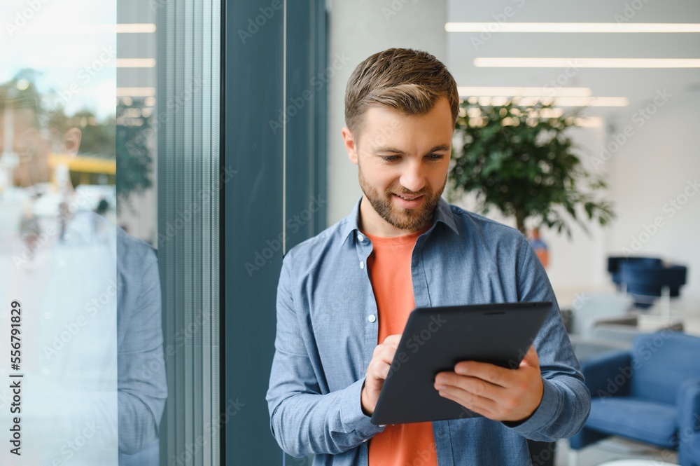 Portrait of young businessman with tablet standing in an office, working. Portrait of young businessman with tablet standing in an office, working.