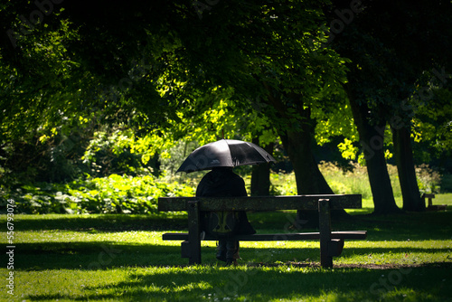 Person in black clothing under a black umbrella in a park on a sunny day, hiding their identity; Hawthorn, Durham, England photo