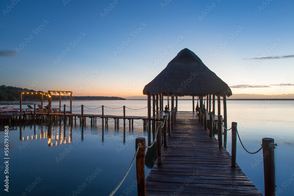 Silhouette of Tiki hut gazebo on dock at Rancho Encantado Eco-Resort & Spa in Bacalar at sunrise; Quintana Roo, Mexico Silhouette of Tiki hut gazebo on dock at Rancho Encantado Eco-Resort & Spa in Bacalar at sunrise; Quintana Roo, Mexico